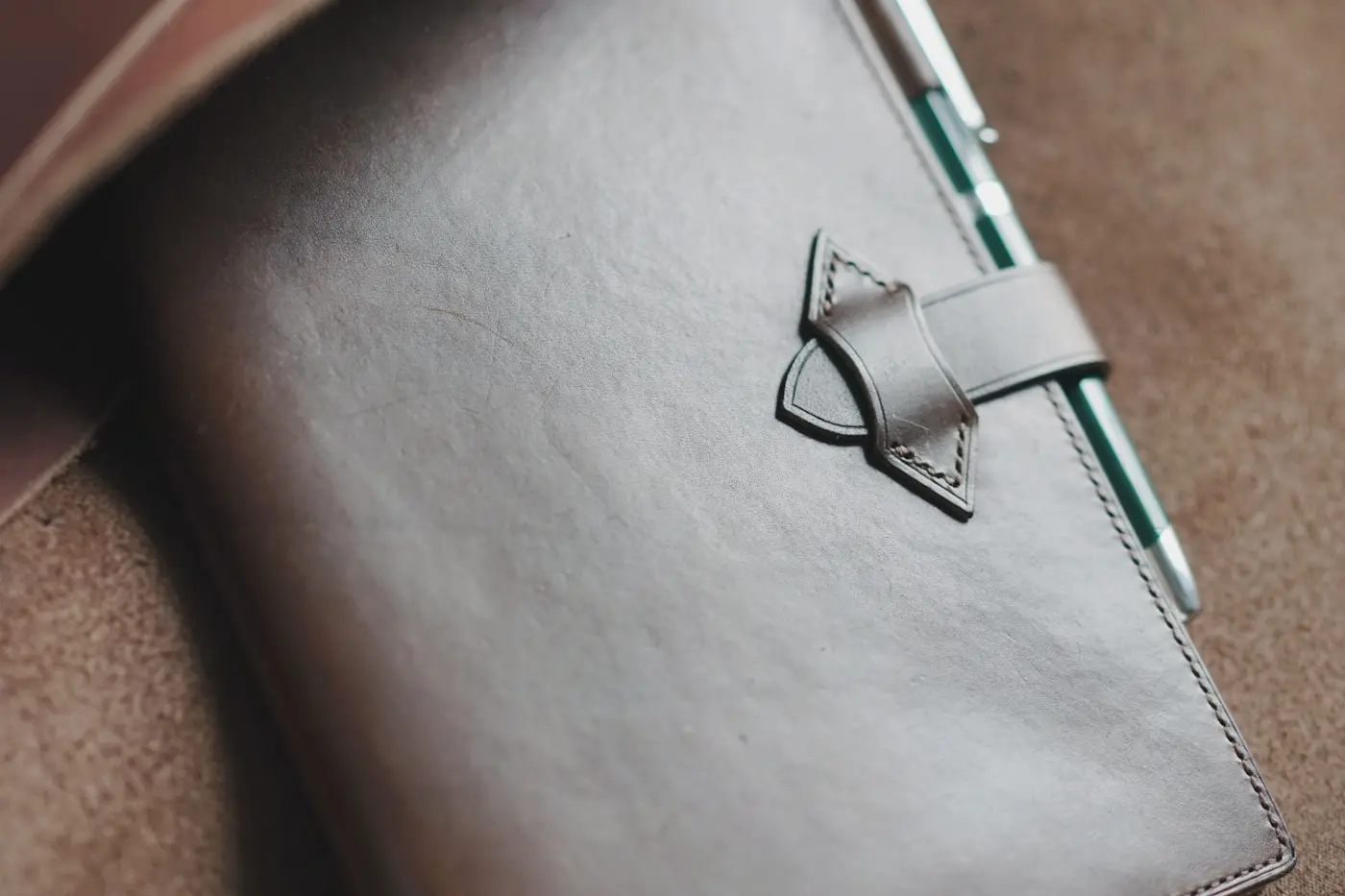 A leather notebook and pen resting on a leather satchel
